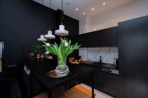 Eine moderne Küche mit schwarzen Schränken, einer Marmor-Spritzschutzwand und einer zentralen Kochinsel mit einem Blumenstrauß.