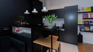 A modern kitchen with black cabinetry, a central island with a vase, pendant lights, and a bookshelf with books and boxes. - ShortStayPoland Orla B61 (Warsaw)