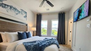 Una camera da letto con un letto, una ventola a soffitto, una televisione e una finestra con tende.
