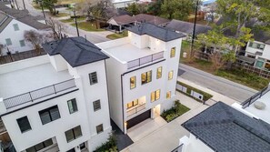 A multi-story residential building with a flat roof, multiple windows, and a visible garage entrance. - Sunhaven Rooftop Villa Gated Retreat with Terrace (Houston)