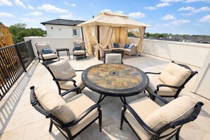 An outdoor patio with a round table, cushioned chairs, and a canopy. - Sunhaven Rooftop Villa Gated Retreat with Terrace (Houston)
