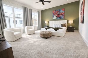 A bedroom with a bed, two chairs, a nightstand, a ceiling fan, and a large window. - Sunhaven Rooftop Villa Gated Retreat with Terrace (Houston)