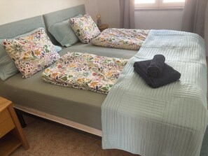 Ein Bett mit blumigem Bettzeug, ein gefaltetes Handtuch und ein Nachttisch mit Lampe.