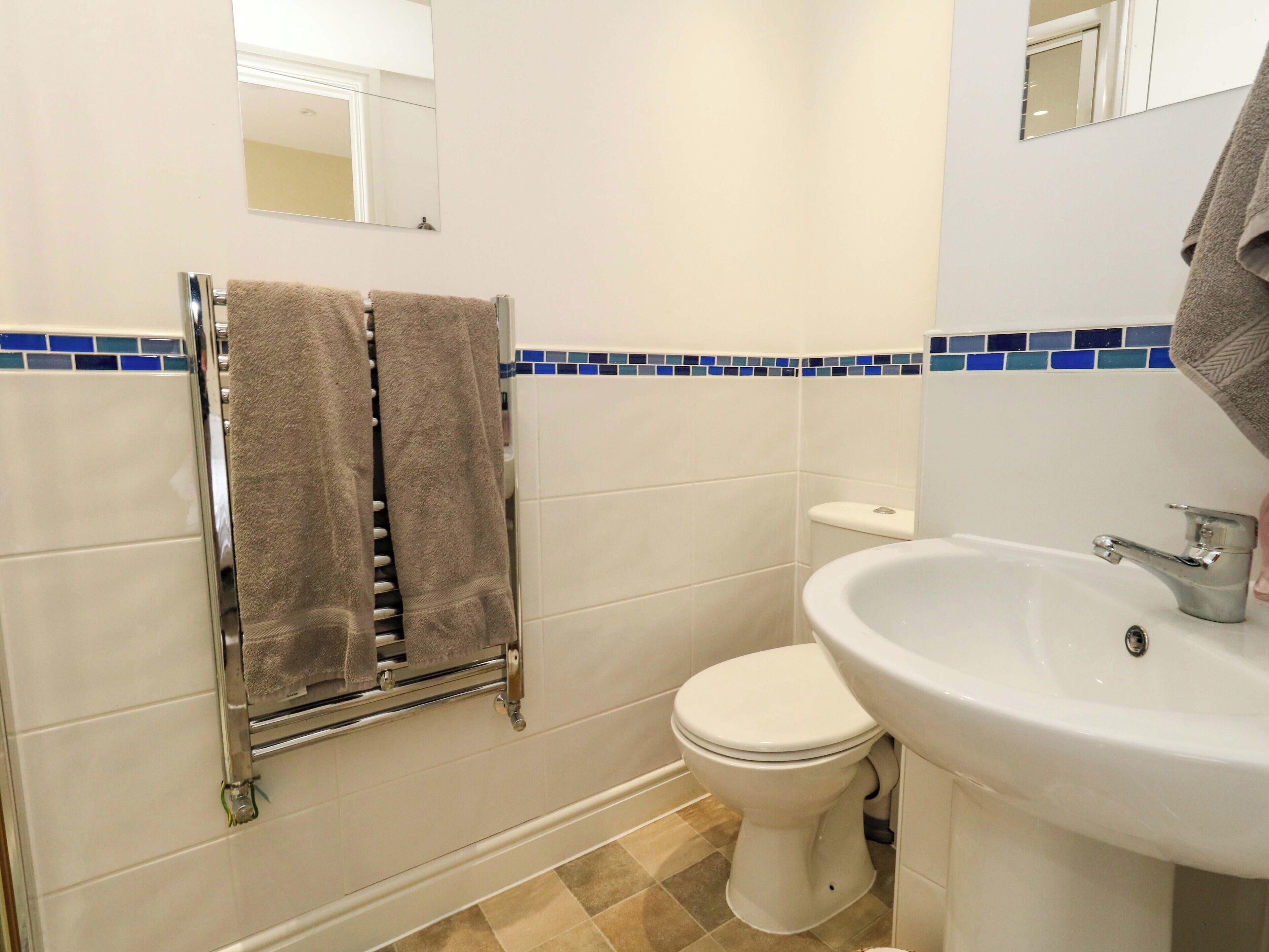 A bathroom with a toilet, sink, towel rack, and blue-tiled backsplash.