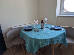 Ein Esstisch mit einer türkisfarbenen Tischdecke, zwei Stühle, einer Weinflasche und einem Salz- und Pfefferset.