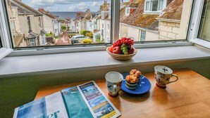 A window with a view of a residential street, a bowl of fruit, and a table with a magazine and two cups. - Seaview Portland (Portland)