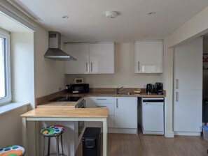 Eine kompakte Küche mit weißen Schränken, einer Mikrowelle, einer Kaffeemaschine und einem Geschirrspüler.