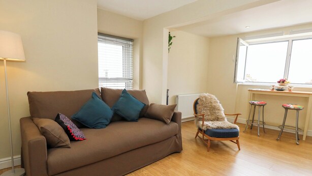 A living room with a brown sofa, a furry chair, and a small kitchen area with stools. - Seaview Portland (Portland)