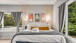 A bedroom with a bed, curtains, wall art, and a view of trees.