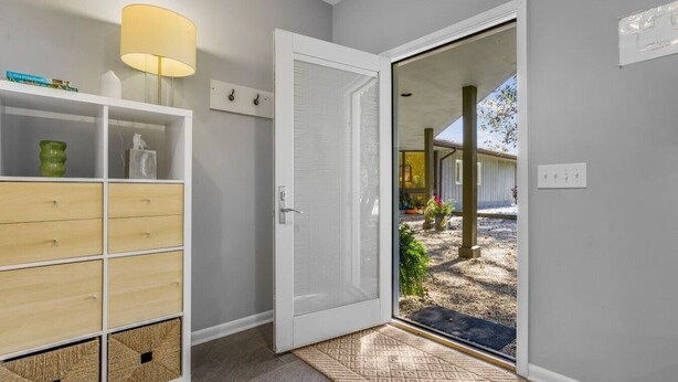 A hallway with a white door, a shelf with storage boxes, a lamp, and a view of the outside.