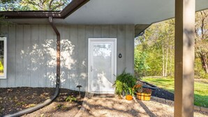 A house with a covered porch, a door, and a garden area with plants and a hose.