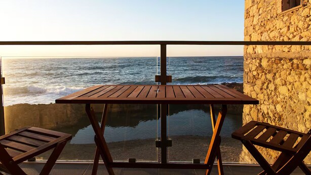 Un balcon avec une table en bois et deux chaises, donnant sur la mer.