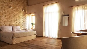 Une chambre avec un mur en briques, un lit, une table de chevet, une chaise et une fenêtre avec des rideaux.