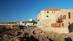 Un bâtiment situé sur la côte, avec des murs en pierre, un toit recouvert de tuiles rouges et un balcon.