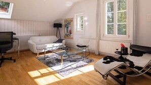 A room with a white sofa, a glass coffee table, a black office chair, a glass table, a black and white lounge chair, a poster, and a window with curtains. - Art Apartments Bern (Bern)