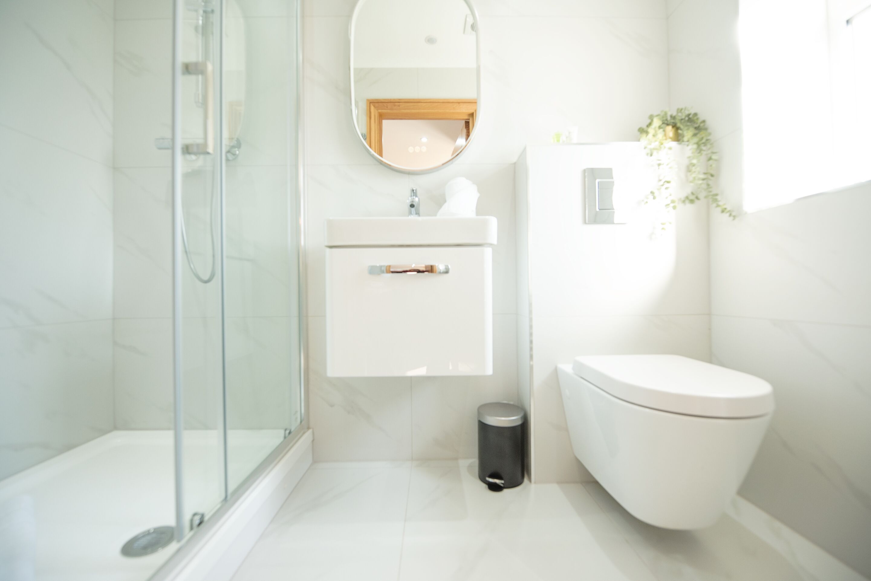Une salle de bain moderne avec une douche à l’italienne en verre, un lavabo blanc avec un miroir au-dessus et des toilettes.
