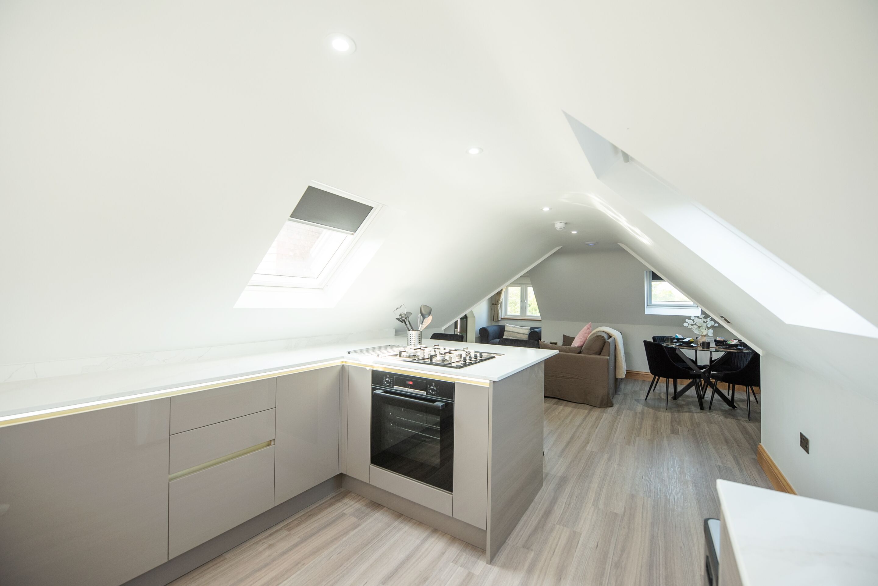Een moderne keuken met een inbouwoven, een eethoek met een tafel en stoelen, en een klein raam.
