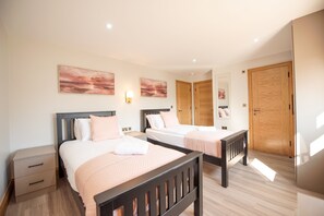 A bedroom with two beds, wooden headboards, a nightstand, a wardrobe, and wall-mounted artwork. - Hazel Lodge (Reading)