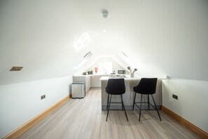 A small, modern kitchen with a white countertop, two bar stools, a microwave, and a small refrigerator. - Hazel Lodge (Reading)