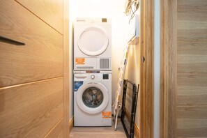 A laundry room with a stacked washer and dryer, wooden cabinets, and a metal rack. - Hazel Lodge (Reading)