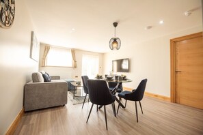 A modern living room with a sofa, dining table, chairs, a TV, and a wooden door. - Hazel Lodge (Reading)