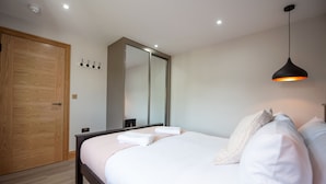 A bedroom with a wooden wardrobe, a large mirror, a bed with white linens, and a pendant light. - Hazel Lodge (Reading)