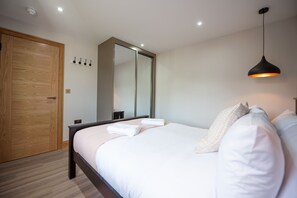 Une chambre avec une armoire en bois, un grand miroir, un lit avec du linge de lit blanc et un luminaire suspendu.