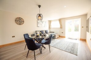 Un coin repas avec une table ronde, des chaises, un luminaire suspendu moderne, une horloge murale et un canapé en arrière-plan.