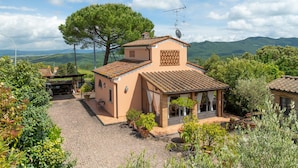 A house with a tiled roof, a large tree, and a view of green hills.
