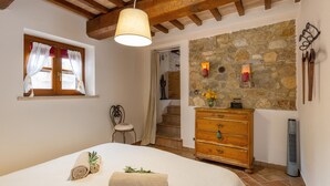 A bedroom with a bed, a wooden dresser, a stone wall, and a staircase leading to another room.