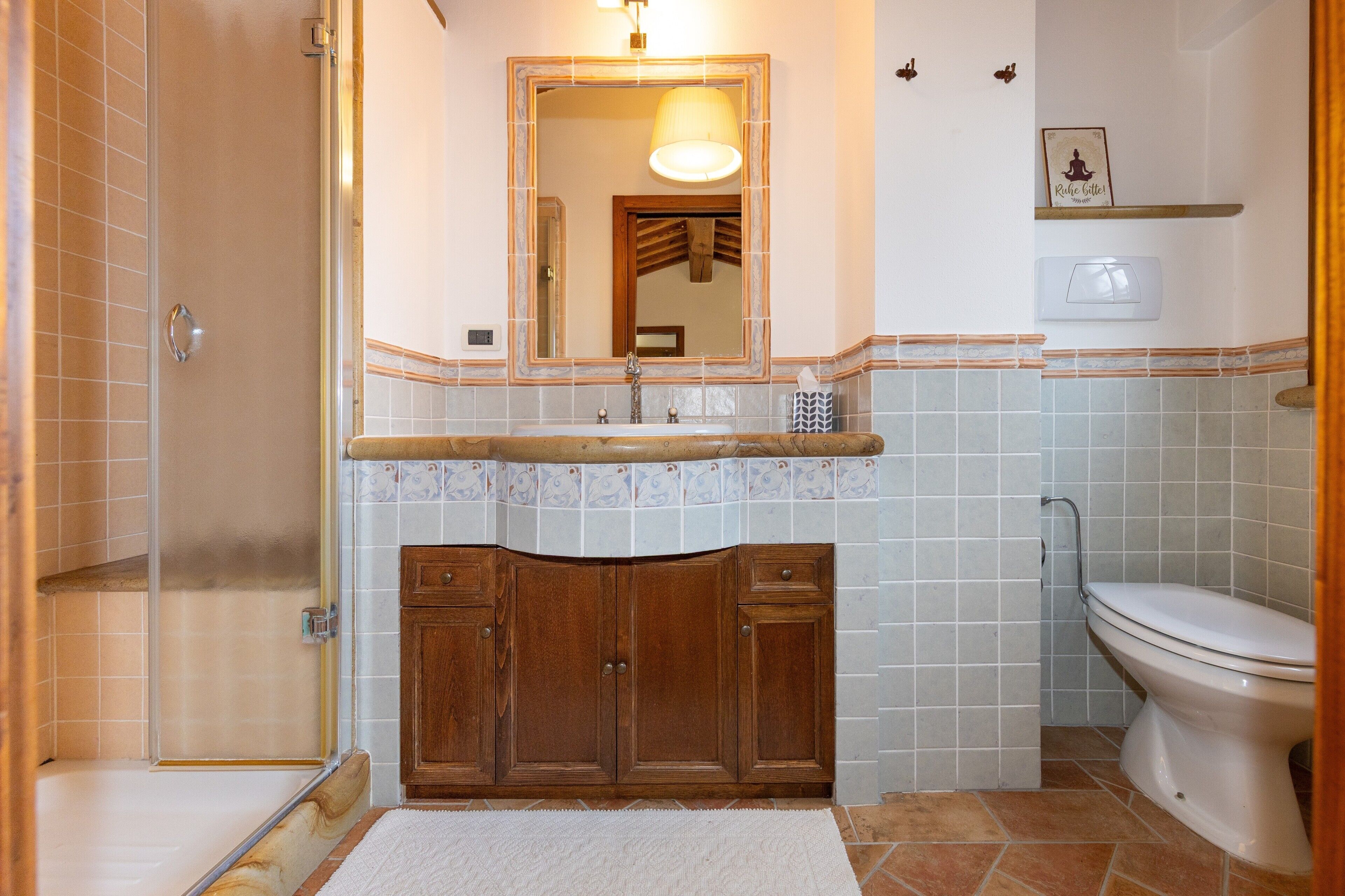A bathroom with a shower, a sink with a mirror, a toilet, and a shelf with a picture.