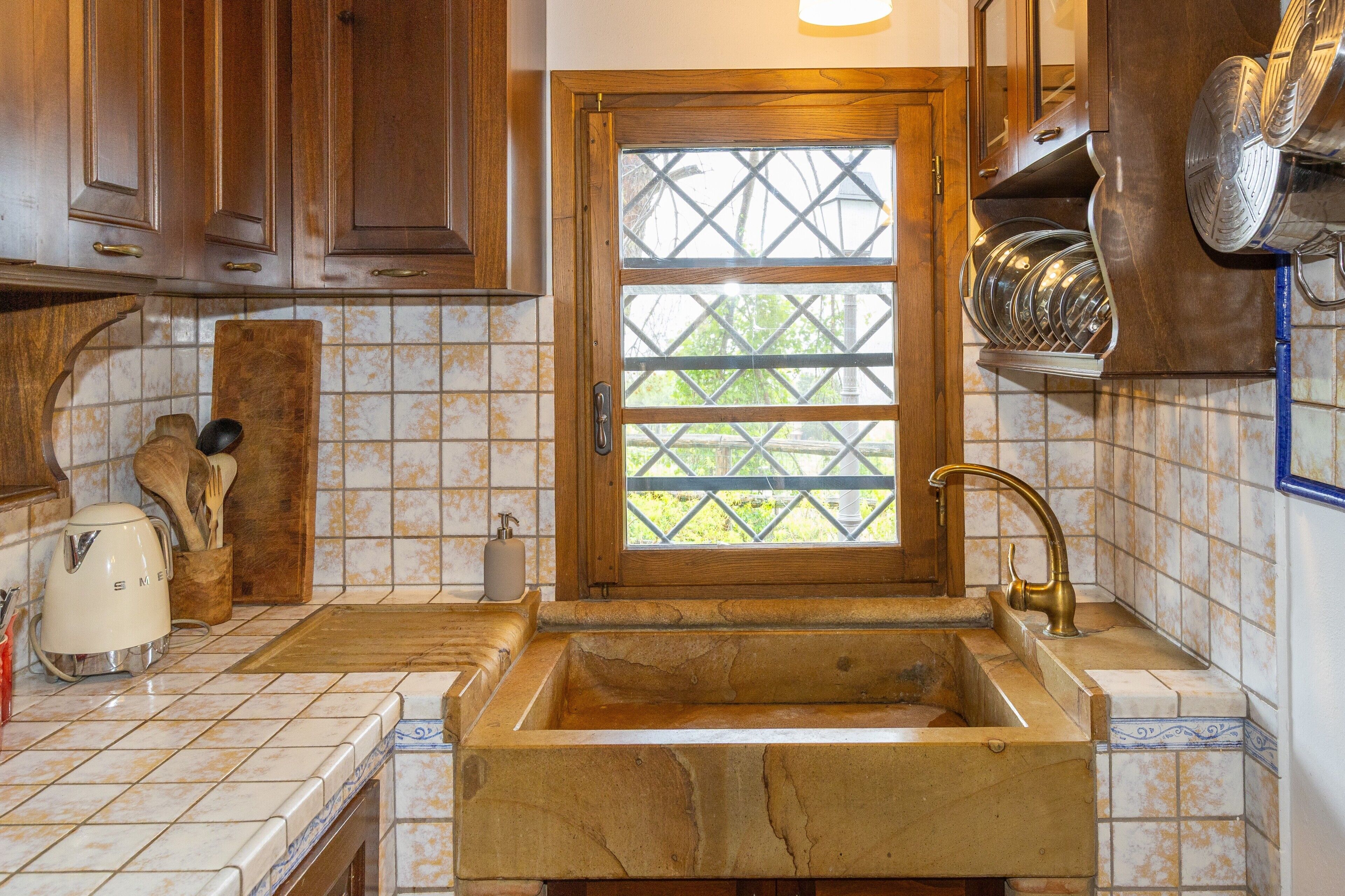A kitchen with a stone sink, wooden cabinets, and a window with a lattice design.