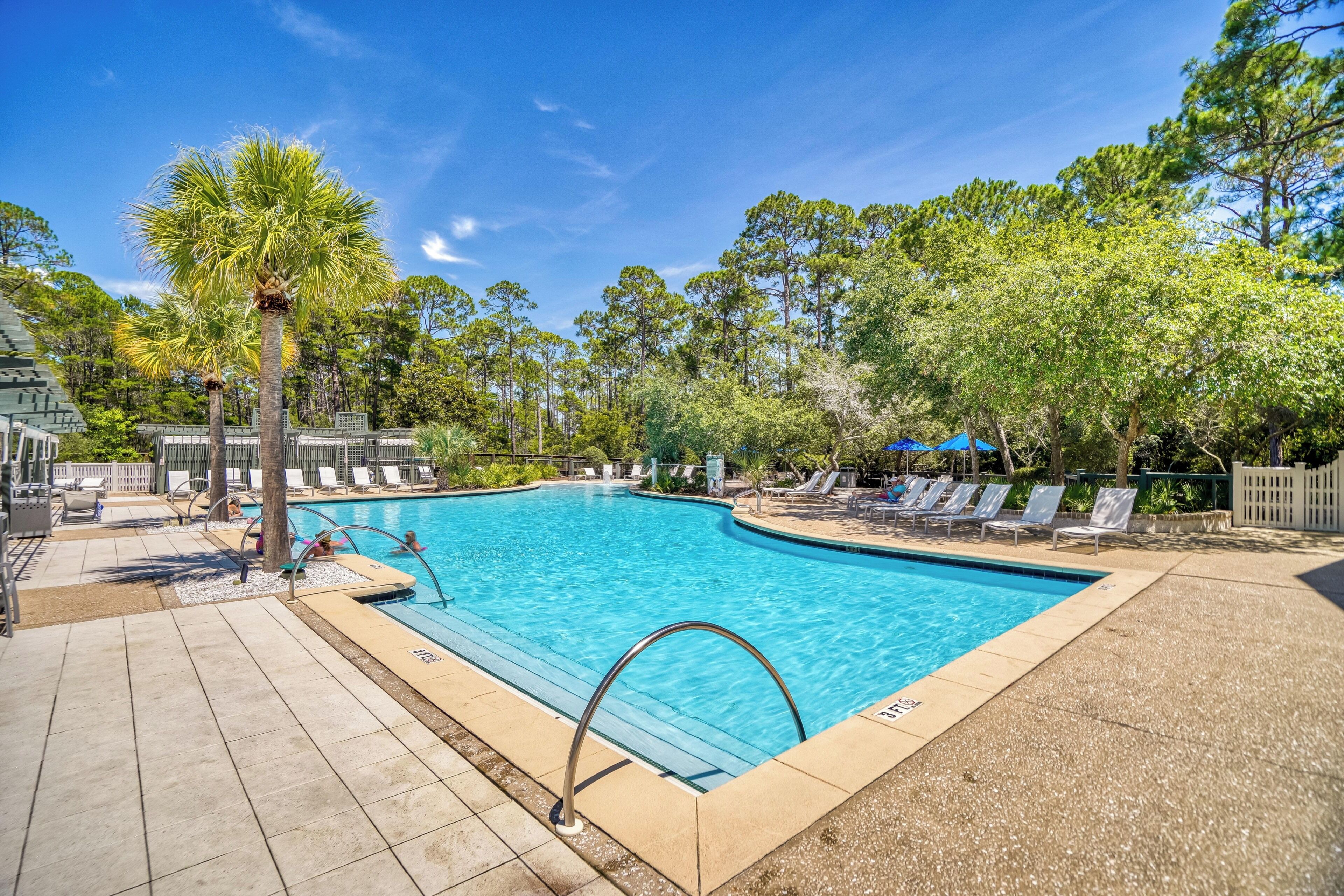 A swimming pool with lounge chairs, palm trees, and a clear blue sky.