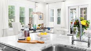 A modern kitchen with a marble countertop, a sink, and a dining area with a table and chairs. - NEW Private Pool, LSV, Bikes, and Carriage House 4 Min to Beach (Santa Rosa Beach)
