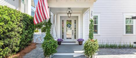 A white house with a front porch, an American flag, and a wreath.