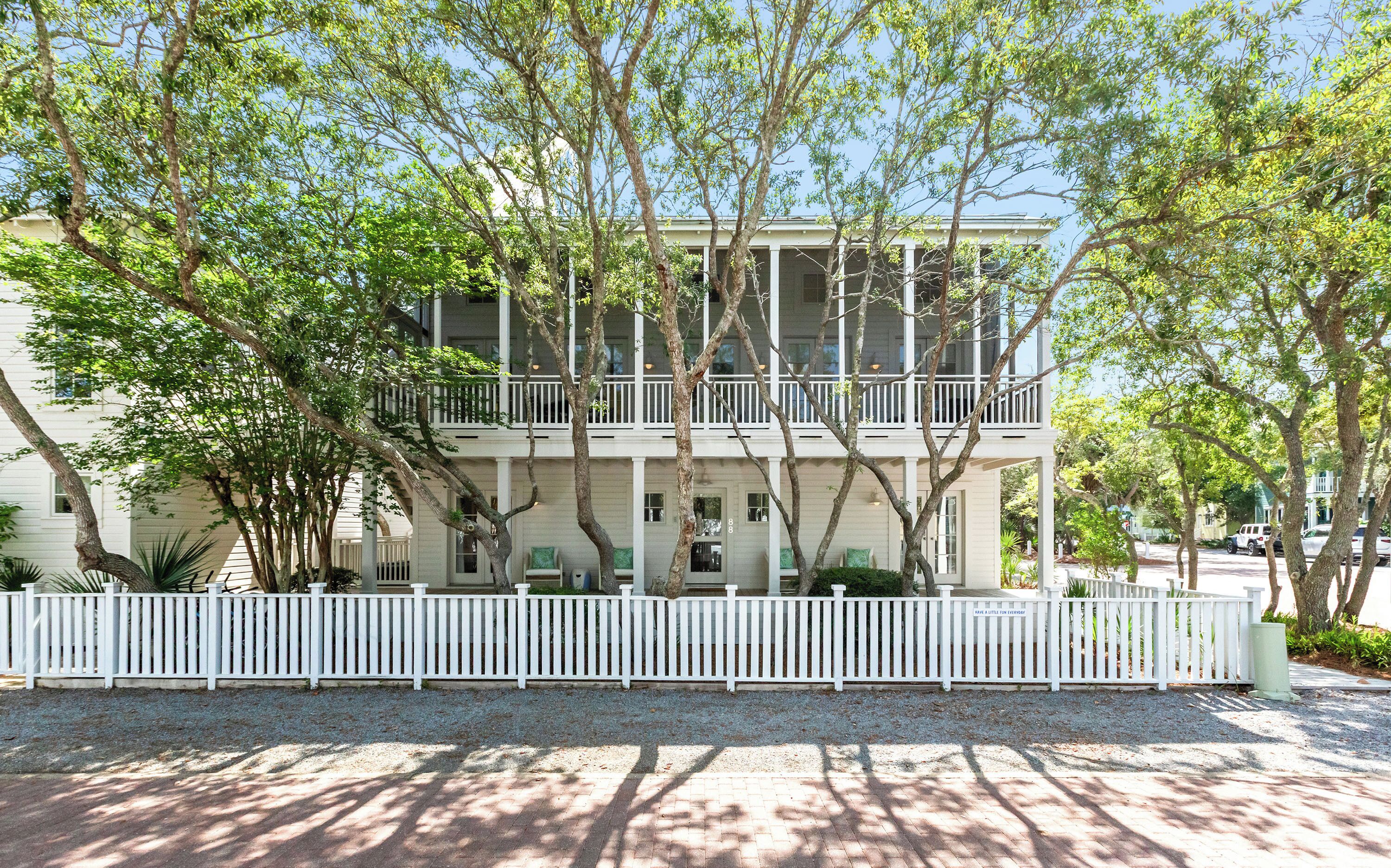 A two-story building with a white exterior, a balcony on the second floor, and a white picket fence in front.