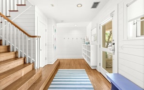 A hallway with wooden stairs, a striped rug, and a view of the outdoors. - NEW Unique Seaside Gem with Gulf Views, Across from Pool, and 1 Block to Beach (Santa Rosa Beach)