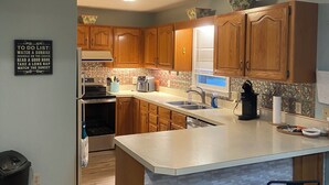 A kitchen with wooden cabinets, a large island with bar stools, a toaster, and a sink. - Quiet Calabash neighborhood convenient to everything (Calabash)