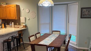A dining area with a wooden table, chairs, a chandelier, and a kitchen in the background. - Quiet Calabash neighborhood convenient to everything (Calabash)