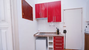 A compact kitchen with a white refrigerator, red cabinets, a countertop with a sink, and a door with a handle. - 1 Bedroom. 1 Washroom. 1 Living Room. 1 Double bed, 1 Sofa bed Apartment (Lisbon)