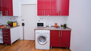 A compact kitchen with a washing machine, microwave, and red cabinets. - 1 Bedroom. 1 Washroom. 1 Living Room. 1 Double bed, 1 Sofa bed Apartment (Lisbon)