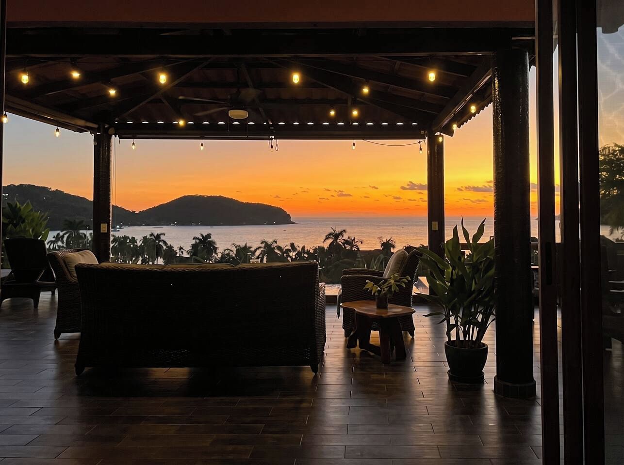 Un espacio de estar al aire libre techado, con vista al atardecer sobre el agua.