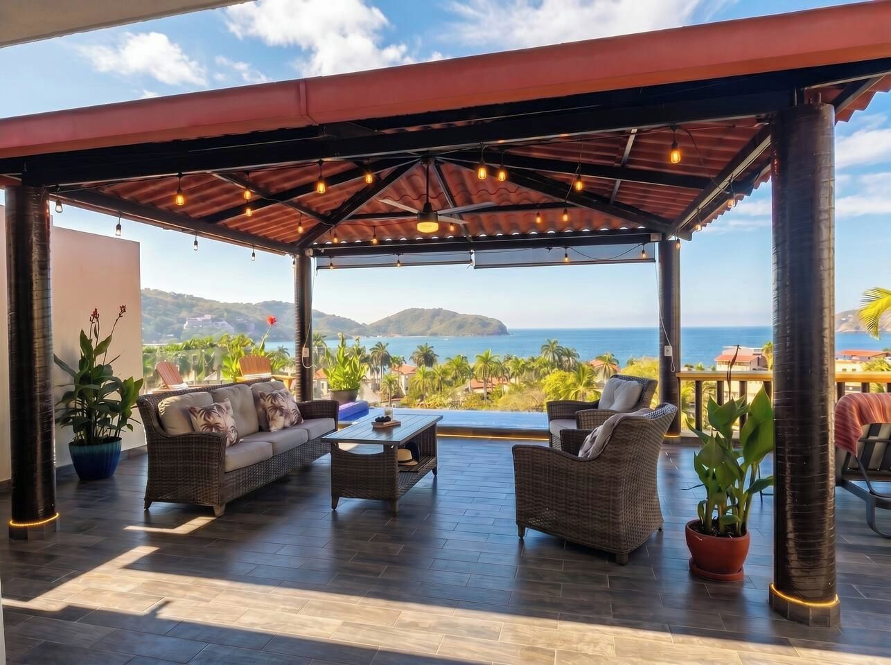 An outdoor seating area with a view of the sea, furnished with wicker sofas and a coffee table.