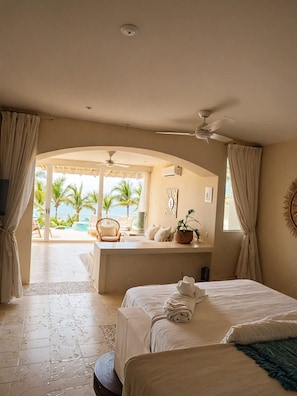 A hotel room with a bed, a seating area with a view, a ceiling fan, and a large window. - Oceanview Suite Perfect Hideaway for Two (La Majahua)