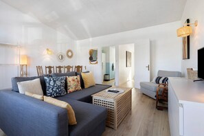 A modern living room with a grey sofa, wooden chairs, a coffee table, and a TV. - Apartment 50 m from the Beach (Audierne)