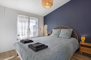 A bedroom with a large bed, a bedside table with a lamp, and a window with curtains. - Apartment 50 m from the Beach (Audierne)