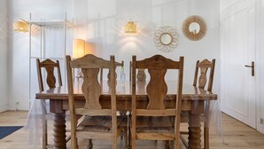 A dining area with a wooden table and chairs, a glass partition, and decorative wall sconces. - Apartment 50 m from the Beach (Audierne)