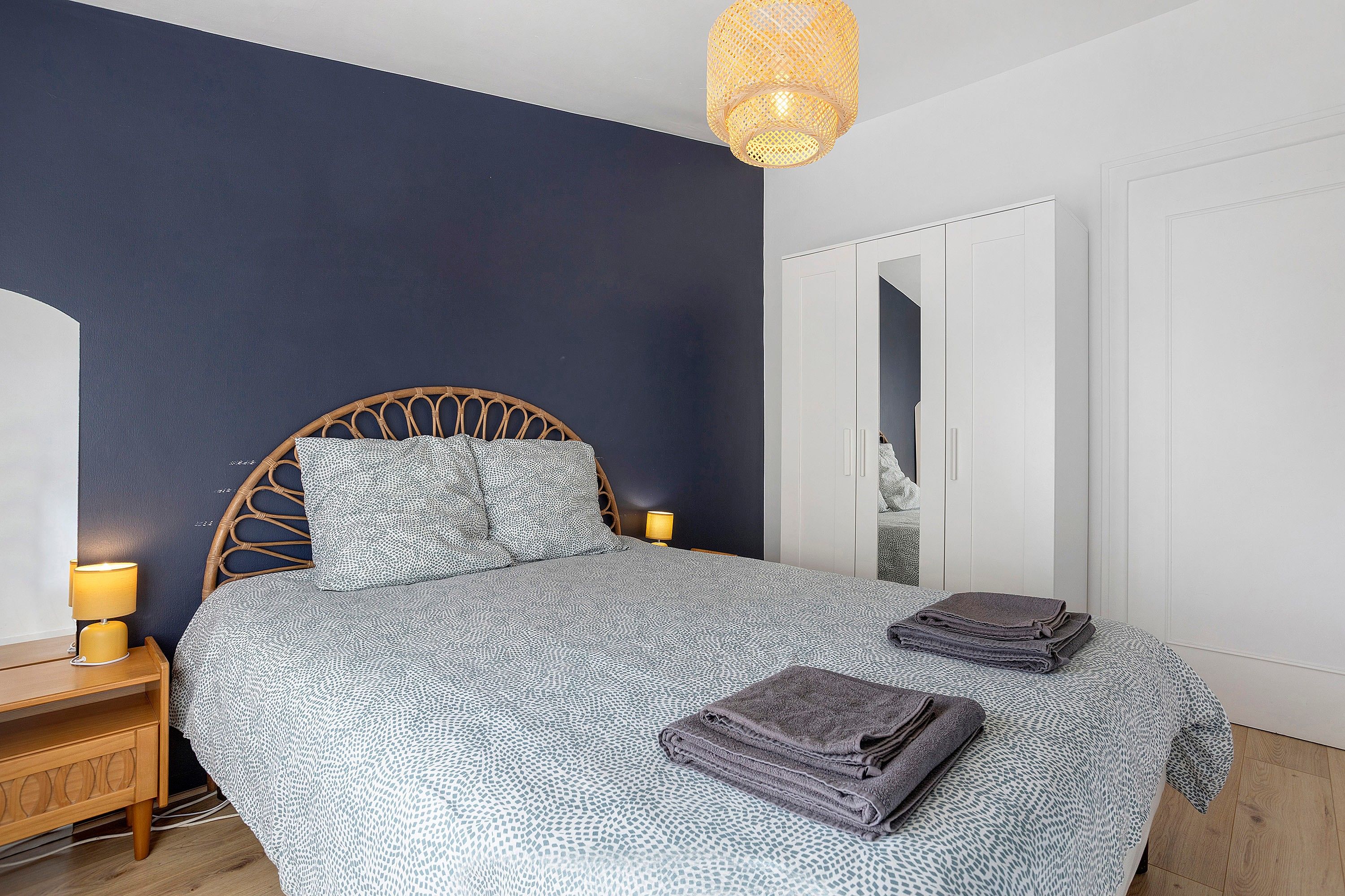 A bedroom with a bed, bedside lamps, a wardrobe, and a hanging light fixture.