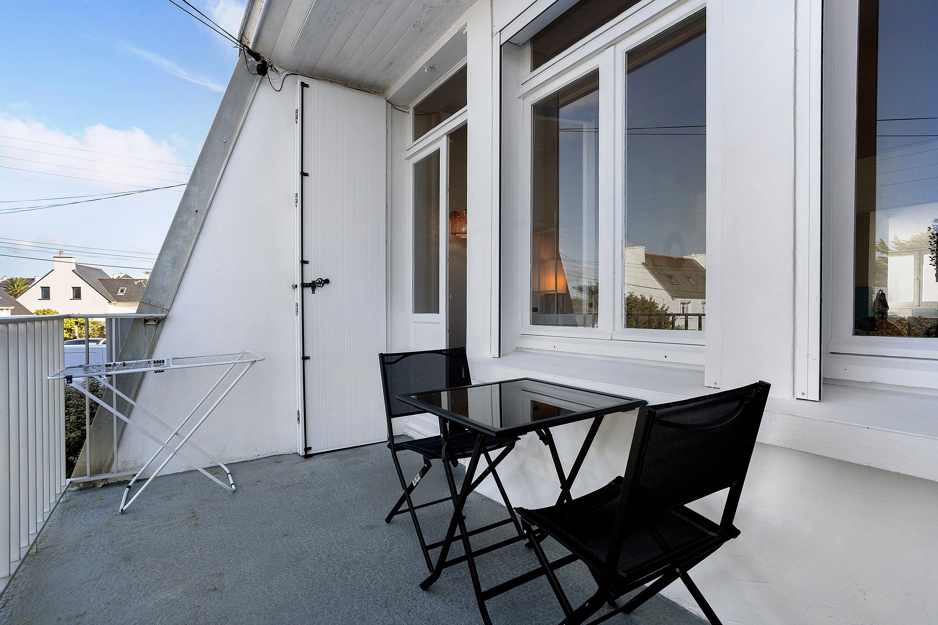 Een balkon met een tafel en stoelen, een droogrek en uitzicht op de omgeving.