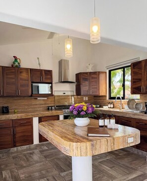Eine moderne Küche mit Holzausstattung, einer Kochinsel, Pendelleuchten und Blick auf Grünflächen.